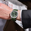 Hand wearing a green PD-YS031 watch with a blurred newspaper background